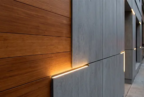 Bina cephesinde gizli lineer aydınlatma ile thermowood ahşap ve fibercement malzeme kombinasyonu uygulamasının detaylı yakın görünümü.